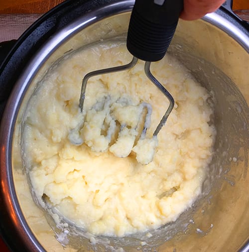 Using a potato masher to mash potatoes that have been cooked in an Instant pot for garlic and ranch mashed potatoes