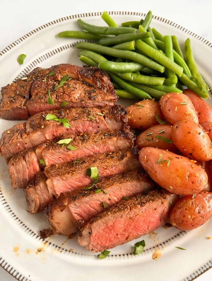 Air fryer ribeye steak on a plate with green beans and potatoes.