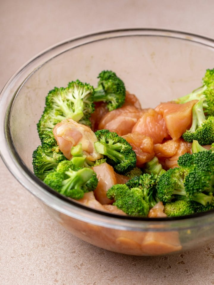 Mixing the broccoli and chicken in a bowl for our sheet pan teriyaki chicken and broccoli recipe.