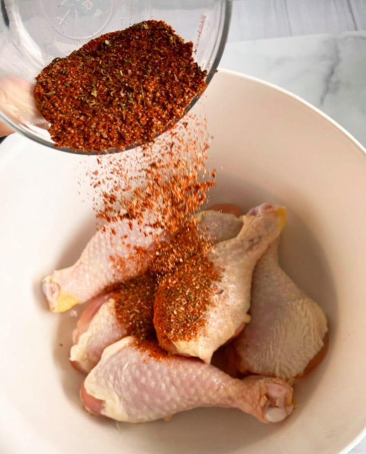 Seasoning chicken legs with blackened seasoning.