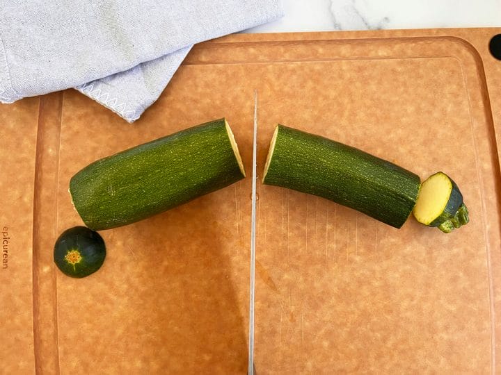 Cutting the ends off a zucchini and cutting it in half.