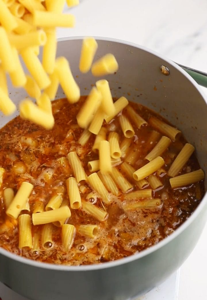Pouring rigatoni into our recipe for one pot pasta with meat sauce recipe.