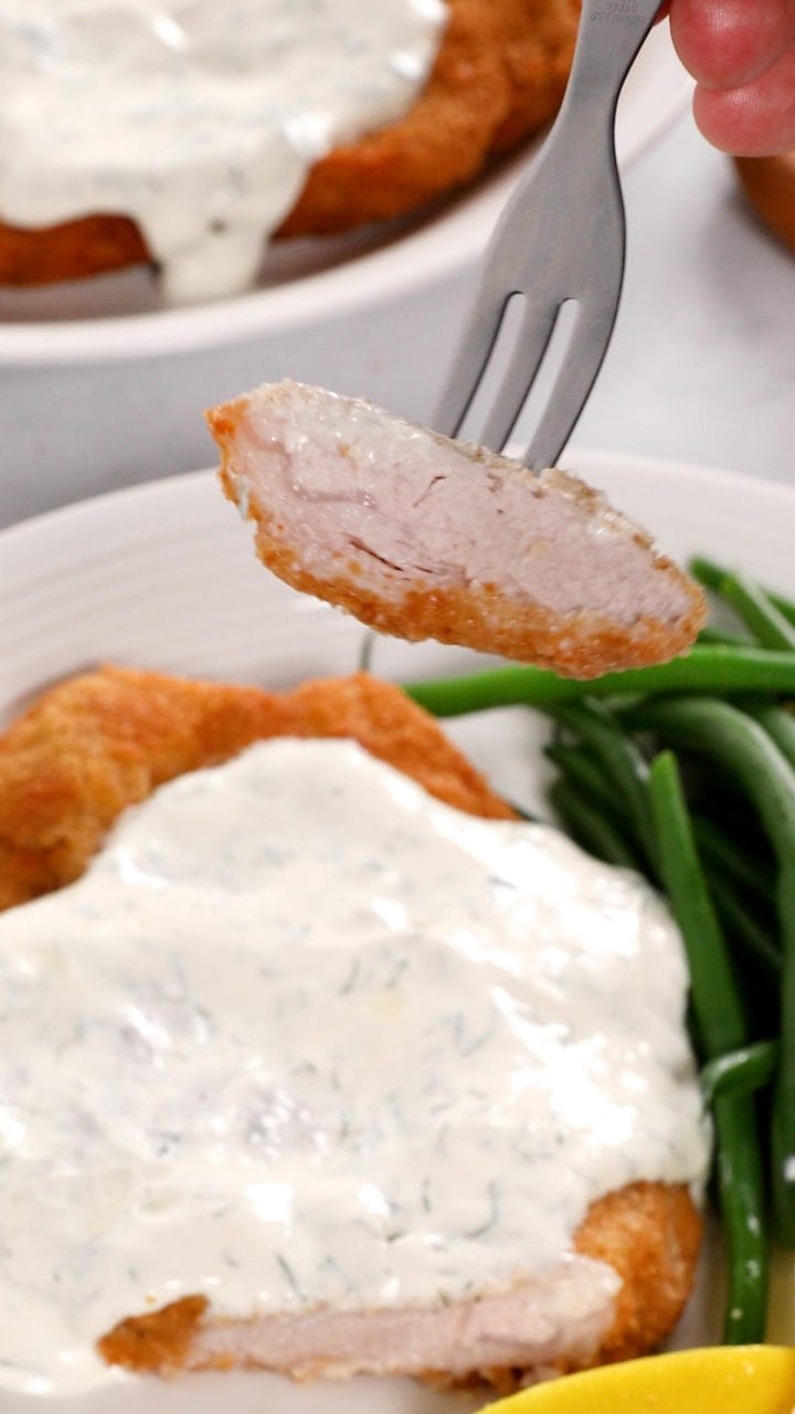 Serving pork schnitzel with creamy dill sauce on a fork.