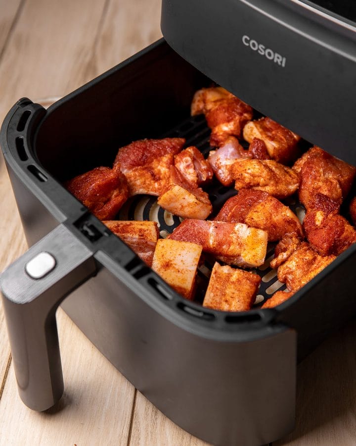 Putting seasoned pork belly bites into an air fryer to be cooked for 15 minutes.