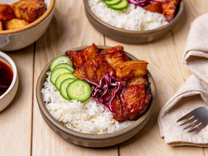 Air fryer pork belly bites served in a bowl with rice, cucumbers and red cabbage.
