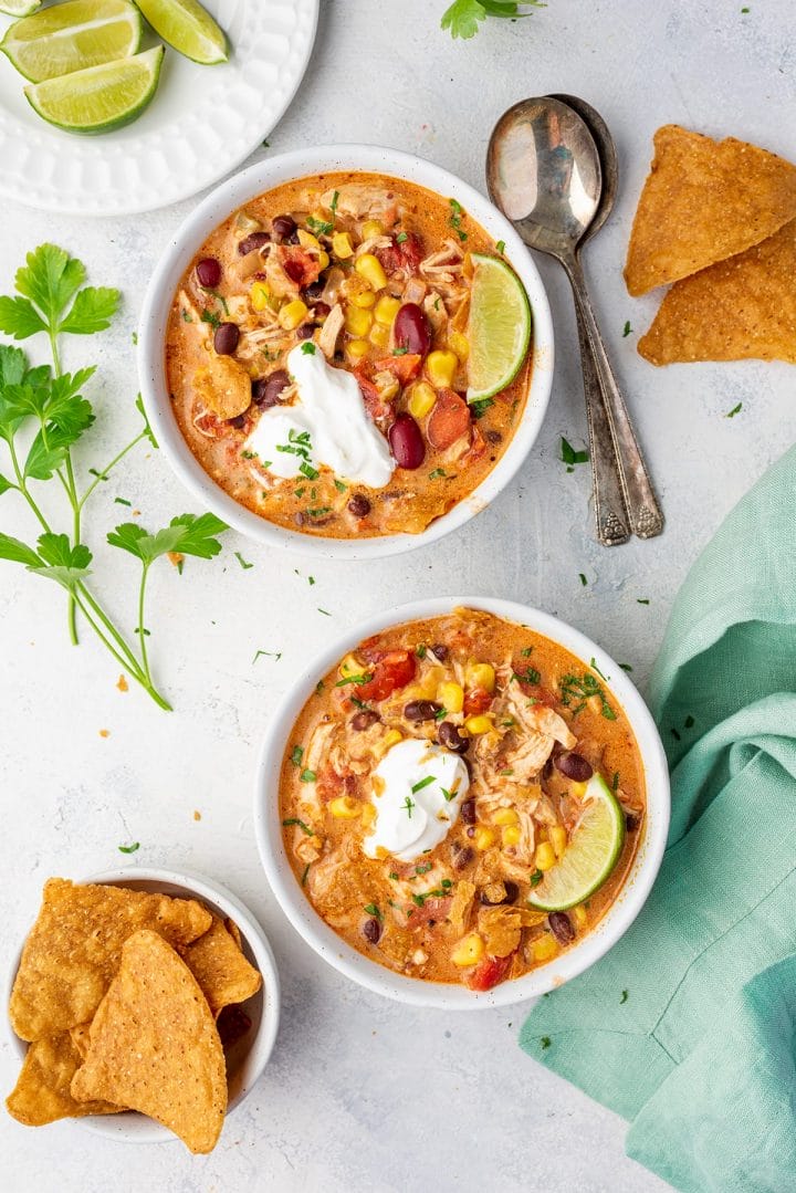 Two bowl of Instant Pot chicken chili served with sour cream, parsley and lime wedges.