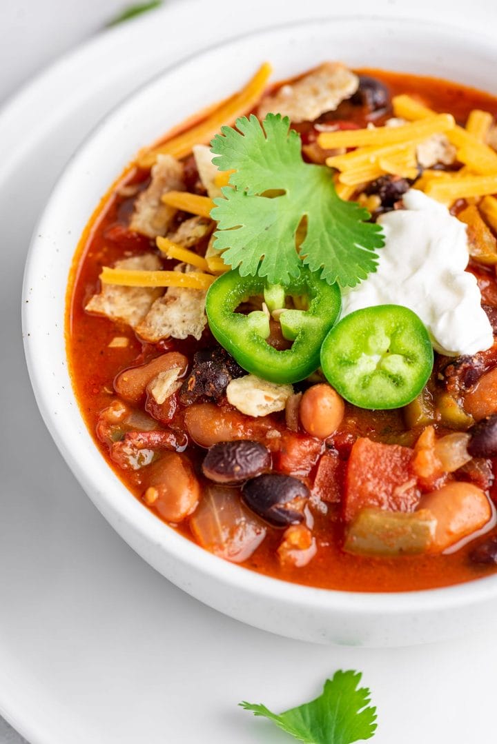 A bowl of Instant Pot vegetarian chili topped with tortilla chips, jalapeños, sour cream and cheese.