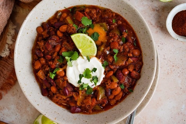 A bowl of chili made in a slow cooker and topped with sour cream, cilantro and lime wedges.