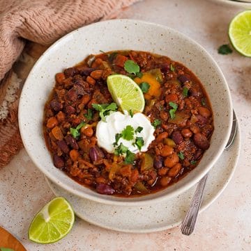 A bowl of slow cooker made chili served with sour cream, cilantro and lime.