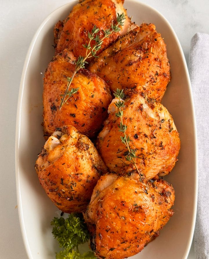 Oven baked chicken thighs served on a platter topped with fresh thyme sprigs. 