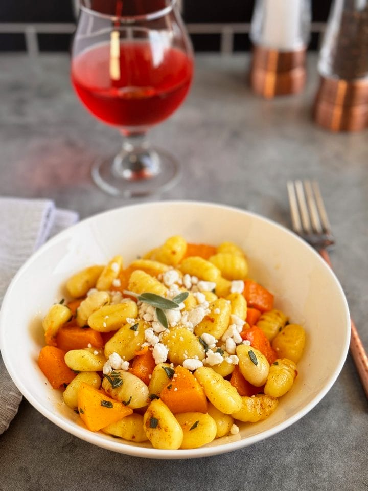 a plate of gnocchi with butternut squash topped with a brown butter sage sauce and goat cheese crumbles.