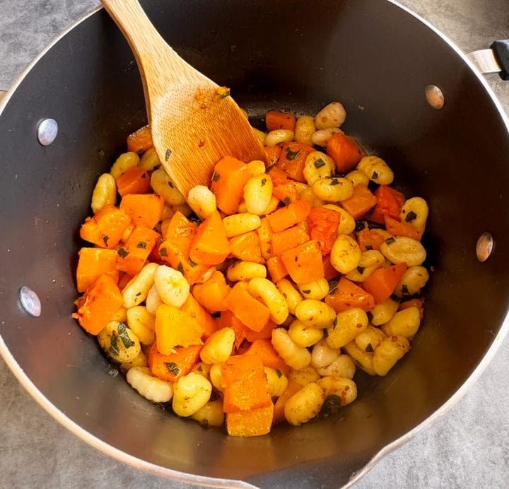Cooked gnocchi and roasted butternut squash being tossed in a pot with brown butter sage sauce.