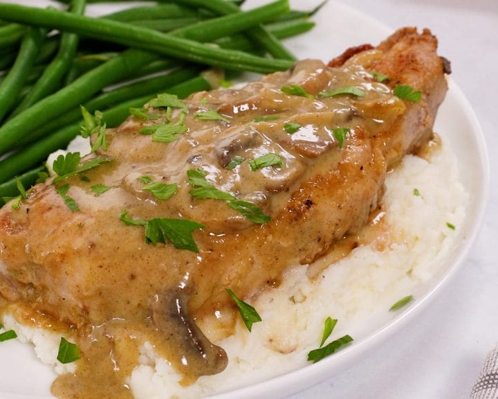 A smothered pork chop served atop mashed potatoes with a side of green beans.
