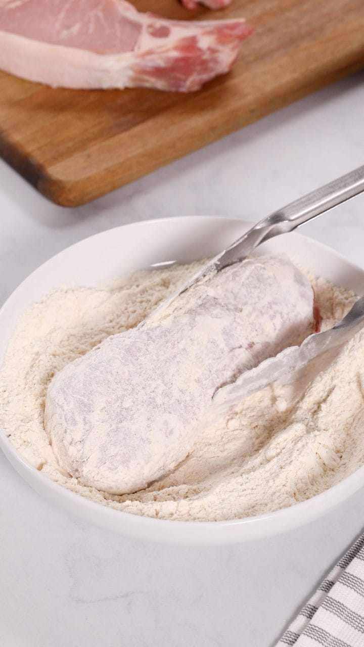 Dredging pork chops through seasoned flour to make smothered pork chops.
