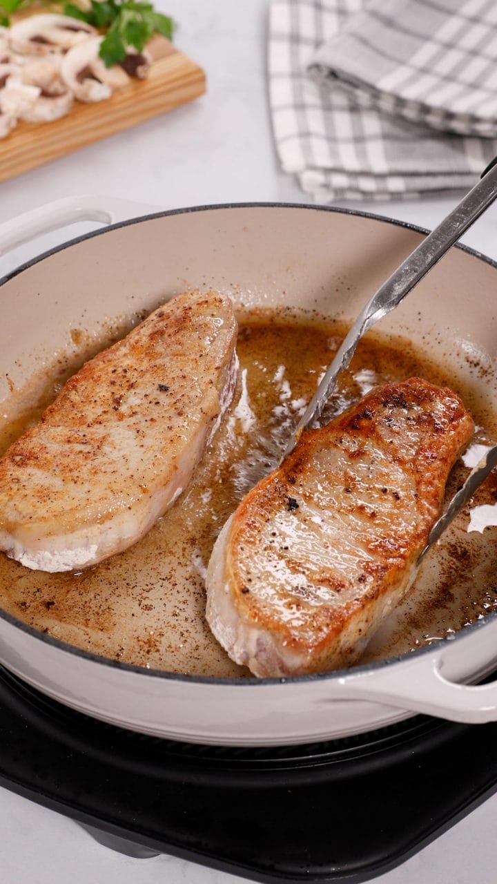 Searing pork chops in a pan until golden brown.